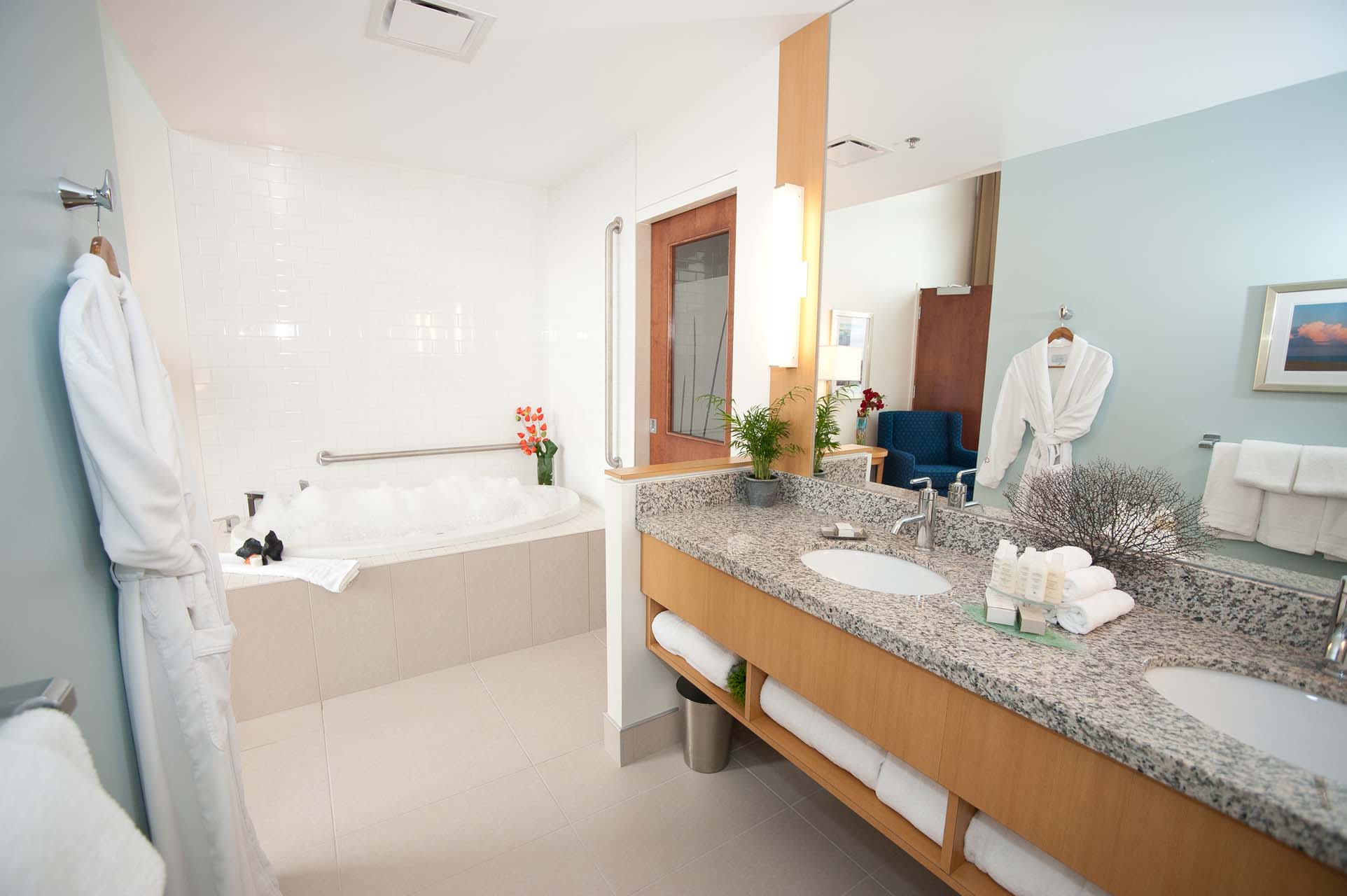 A bathroom with double sinks, a tub, and a bathrobe hanging on the wall