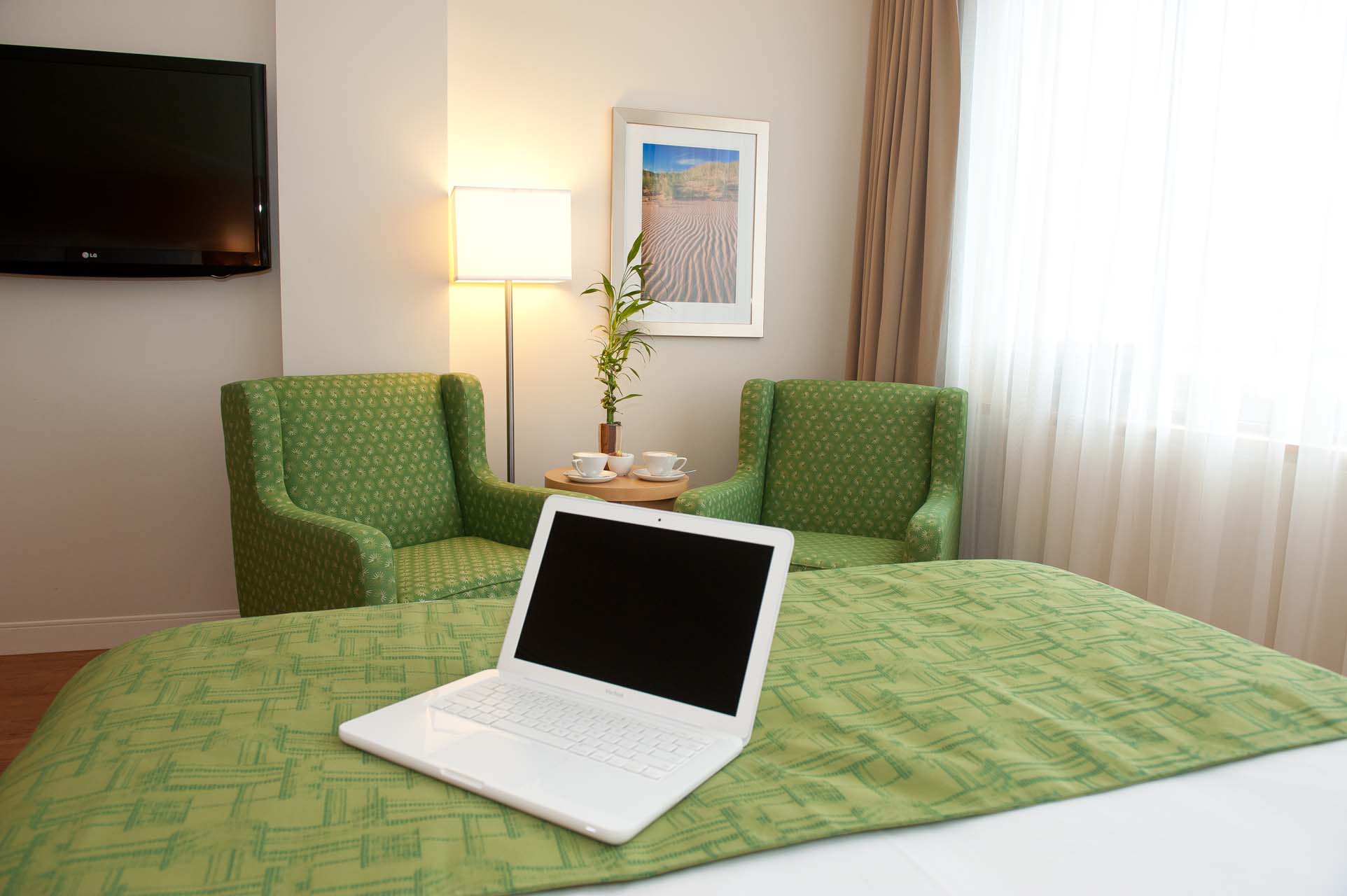 A laptop open on a queen bed with two armchairs in the background