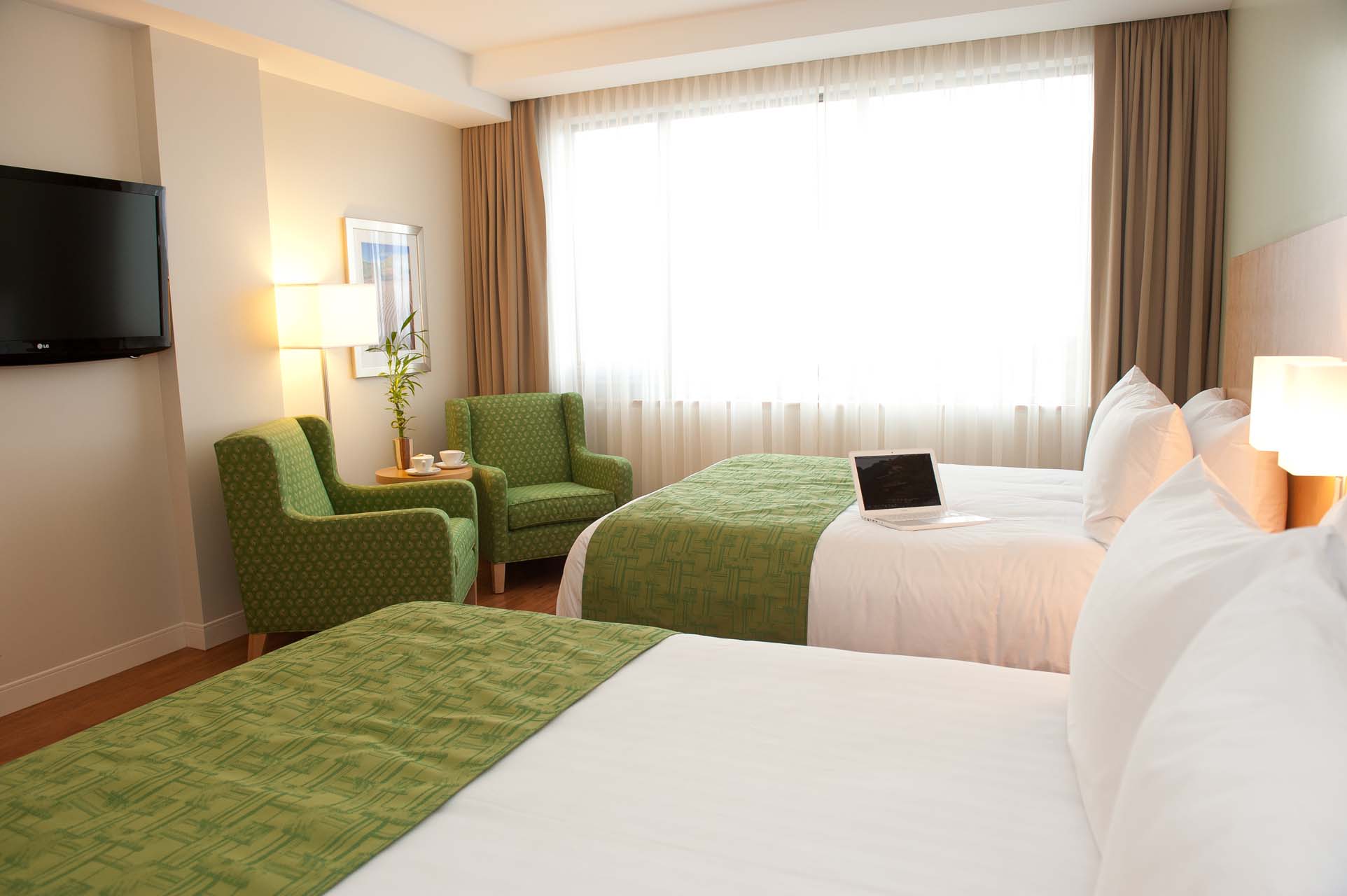 Two queen beds, two armchairs, and a wall-mounted TV in a guest room