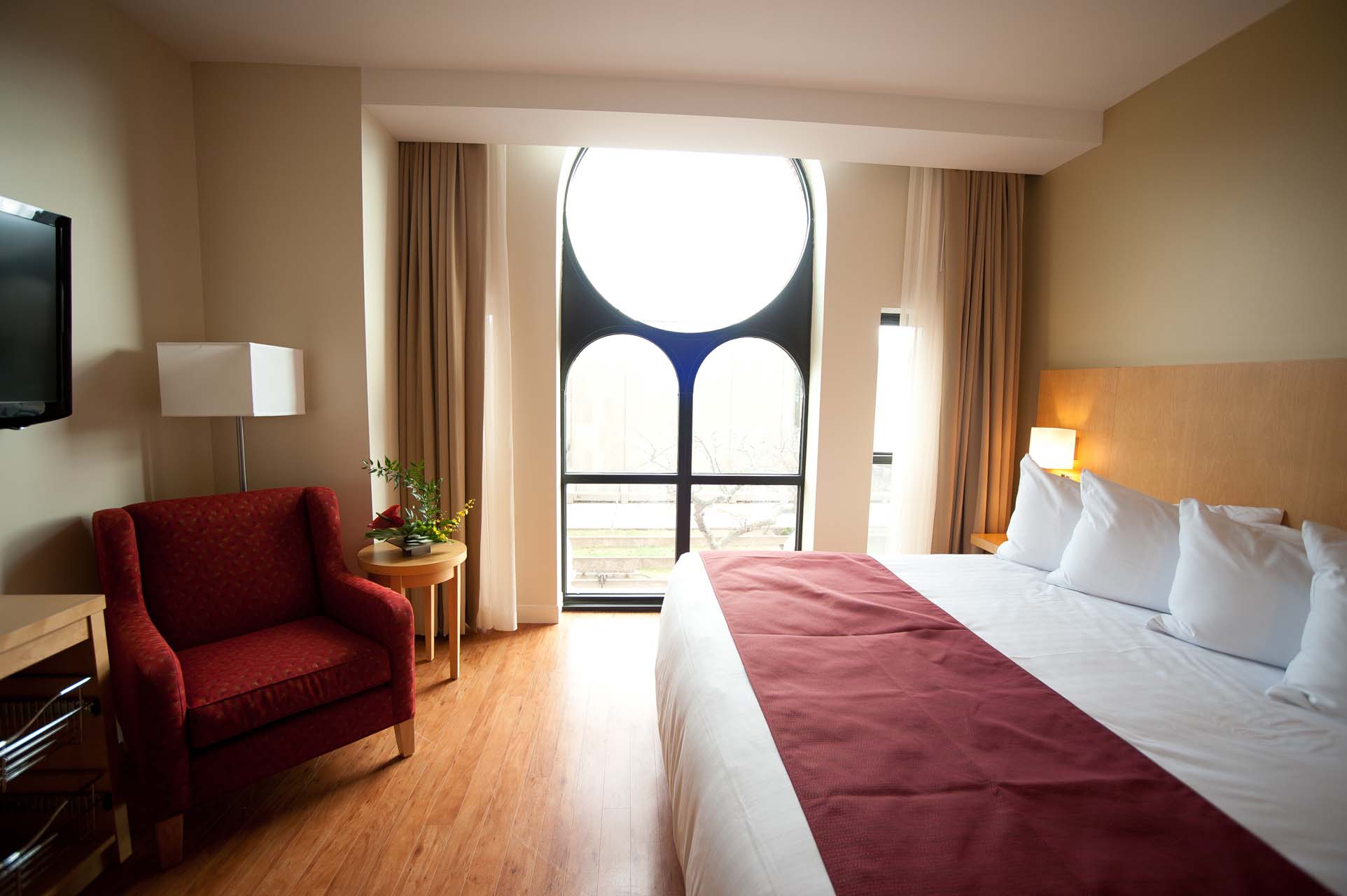 A guest room with a king bed, an armchair, and a large window
