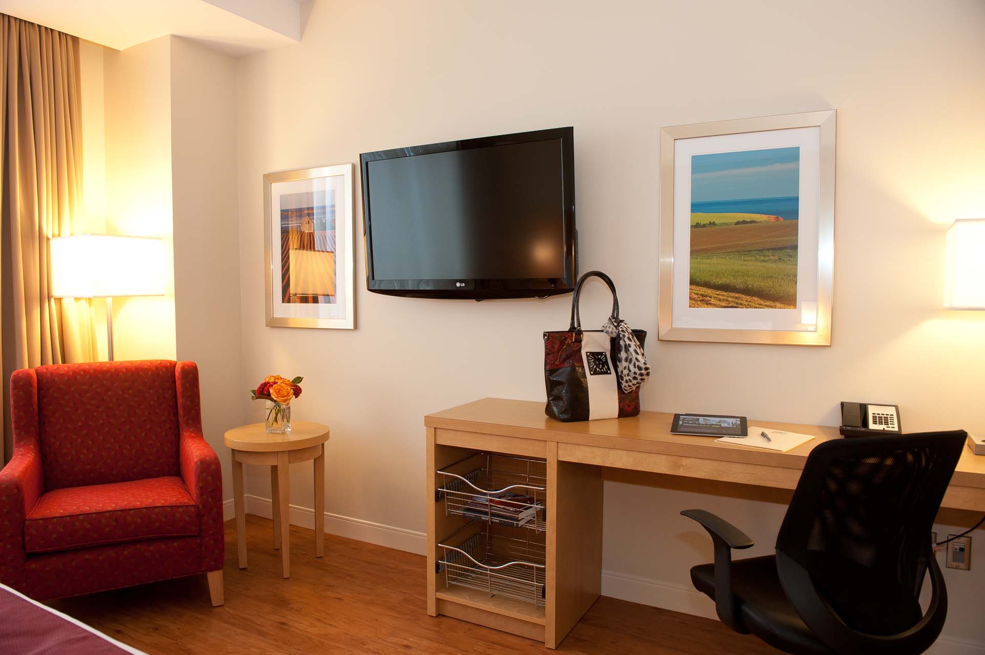 A guest room with an armchair, a wall-mounted TV, and a work desk